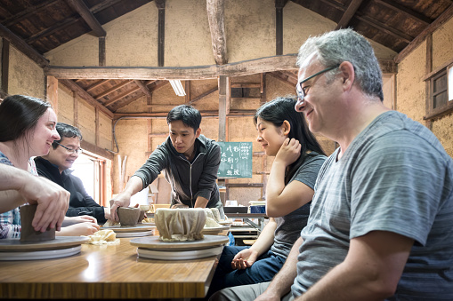 A Japanese man checks the thickness of a student's pot while teaching a traditional Japanese hand built pottery class to a group of multiracial, multigeneration family and friends in Nara, Japan.