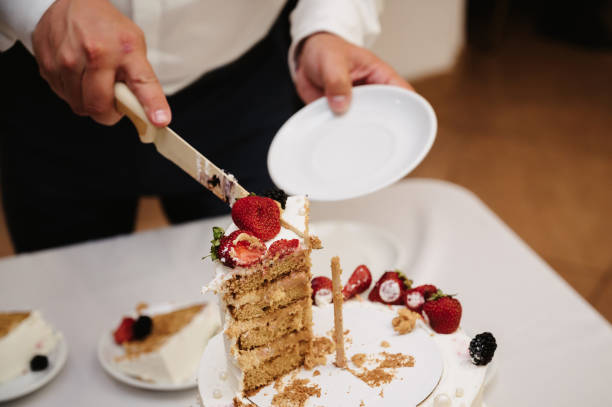 istock groom's hand cuts the wedding cake into pieces 2148350250