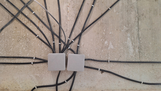 Many black electrical wires are attached to a gray concrete surface. The cables converge into junction boxes. Background.