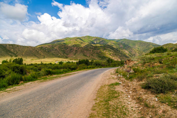 istock country road with mountains, grass, and clouds in the background 2148351580
