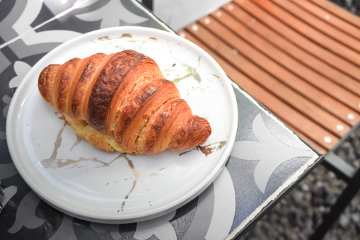 A plain butter croissant on white ceramic plate on tiled table. Concept for breakfast, restaurant and eatery.