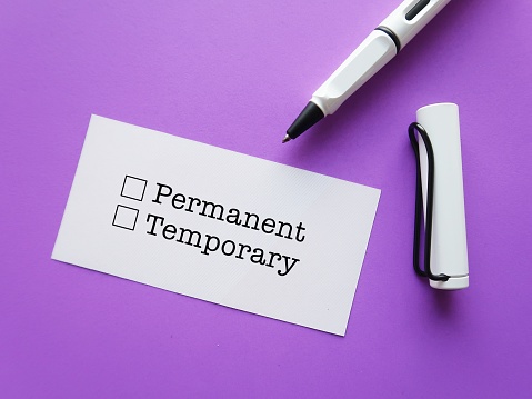 Paper note on purple background with pen ticking on choices PERMANENT (no end date which employee receives benefits package) or TEMPORARY (duration of employment with contract end date) employment