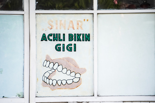 Yogyakarta, Indonesia - December 29, 2023: Old fashioned Denture maker's workshop advertisement in Jogja city. Dental expert shop selling and making false imitation teeth.