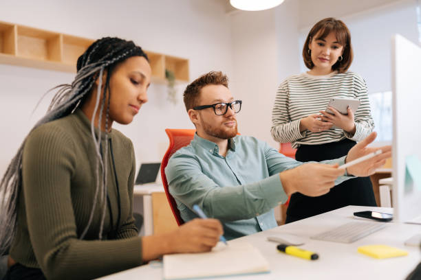 istock Focused male mentor or executive manager boss teaching diverse female internes, explaining work pointing at computer screen. Team leader supervisor training 2148354360