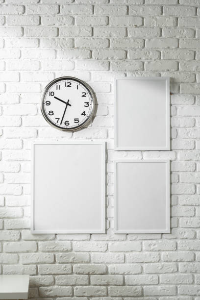 minimalist white wall decor featuring a clock and blank photo frames - customisable fotografías e imágenes de stock