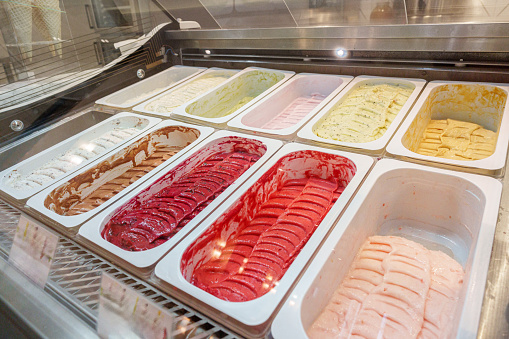A variety of gelato flavors are neatly arranged in a display case, showcasing vibrant colors and tempting textures that indicate a rich, creamy dessert experience at an Italian ice cream parlor.