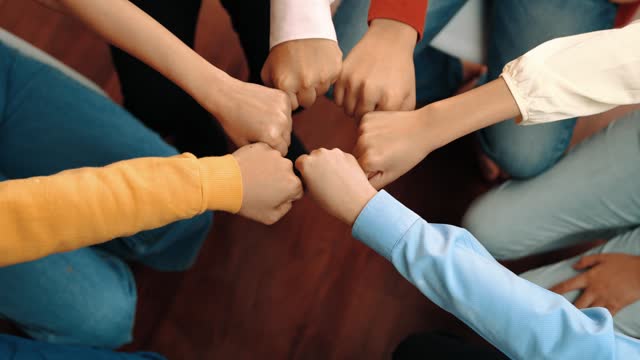 Employee group in casual wear sit around friendly fist bump assemble. Synergic