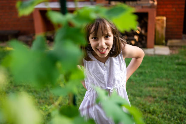 Happy little girl standing in the yard at summer and looking at camera