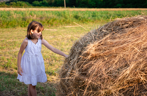 Happy girl standing next to hay stack in the village at summer
