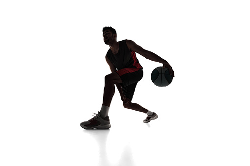 Silhouette of concentrated male athlete, basketball player in motion, dribbling ball isolated on white background. Concept of professional sport, competition, game, tournament, action