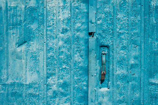 Old door handle and door painted blue. The old surface is painted with blue oil paint. Close-up. Texture. Abstract background