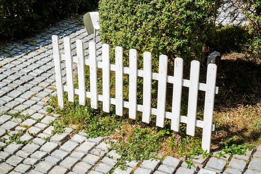 Elegant white garden fence and gate with pink roses, salvia, catmint, lady's mantle flowers and bushes bordering house entrance.