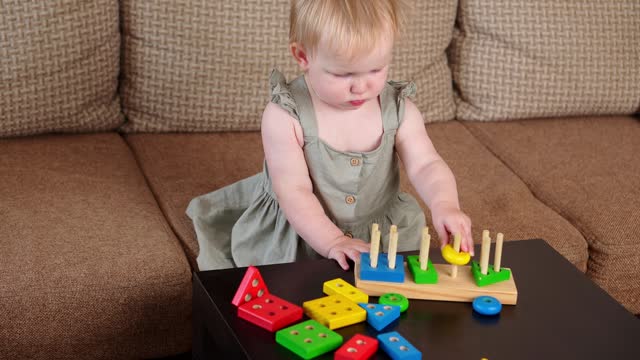 Toddler plays with a wooden educational toy while sitting on the sofa at home. Montessori games for child development. Concept of play, learning and early child development.