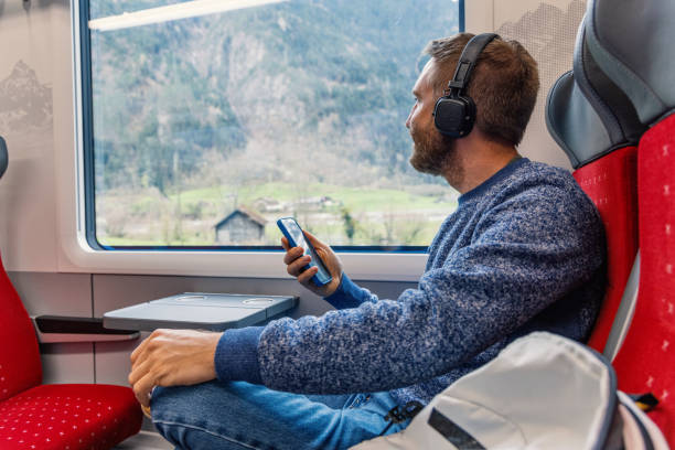 istock Young man on a train listening to music on his mobile device while enjoying nature 2148365771