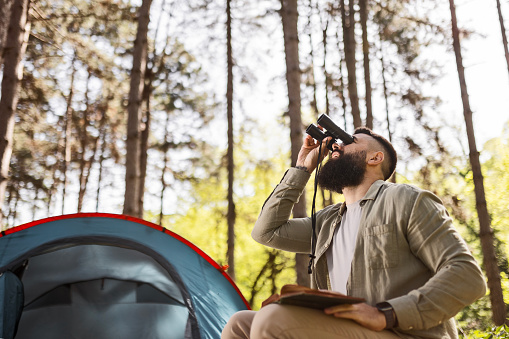 Young man sitting next to tent camping bird watching
