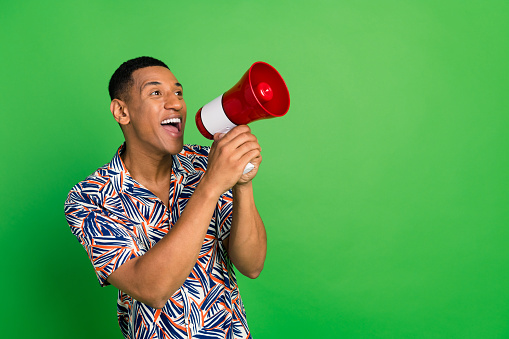 Photo of cheerful person look communicate loudspeaker toa empty space isolated on green color background.