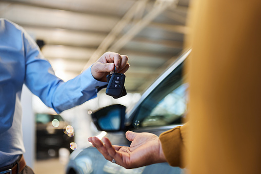 Close up of unrecognizable salesman giving car keys to his black customer in a showroom.