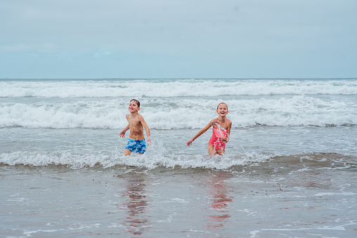 Siblings playing on beach, running, having fun. Smilling girl and boy on sandy beach of Canary islands. Concept of a family beach summer vacation with kids.