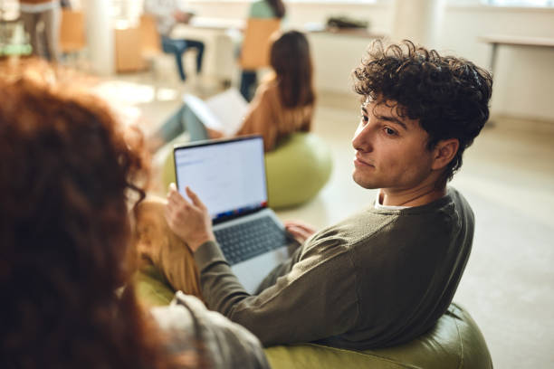 Male student talking to his friend while e-learning at casual classroom.