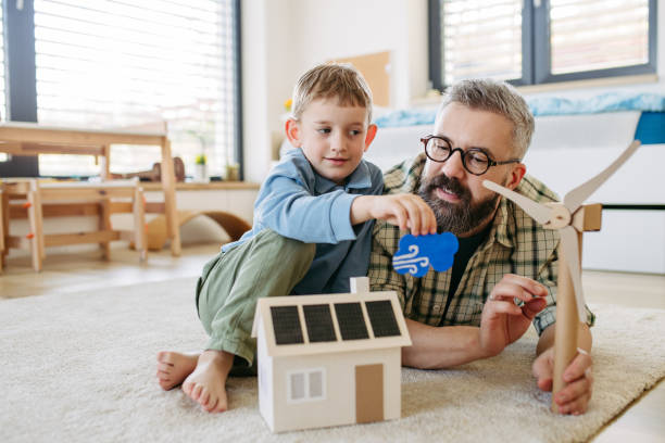 istock Father explaining renewable energy, teaching about sustainable lifestyle his young son. Playing with house with solar panels, wind turibine at home. 2148371239