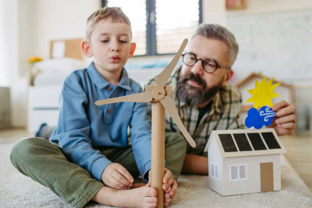istock Father explaining renewable energy, teaching about sustainable lifestyle his young son. Playing with house with solar panels, wind turibine at home. 2148371531