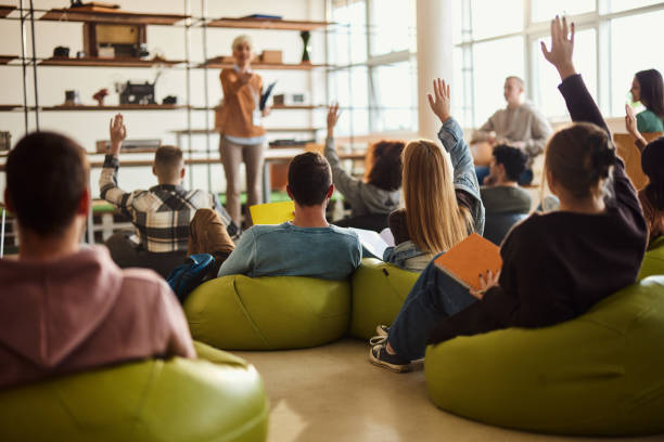 istock Rear view of students raising hands on a class at casual classroom. 2148371573