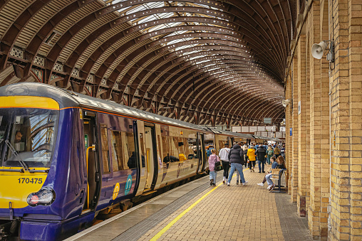 York, UK.  April 7, 2024.  A train has arrived at a railway station platform. Passengers have disembarked and are walking off the platform.  A curving iron canopy is above.
