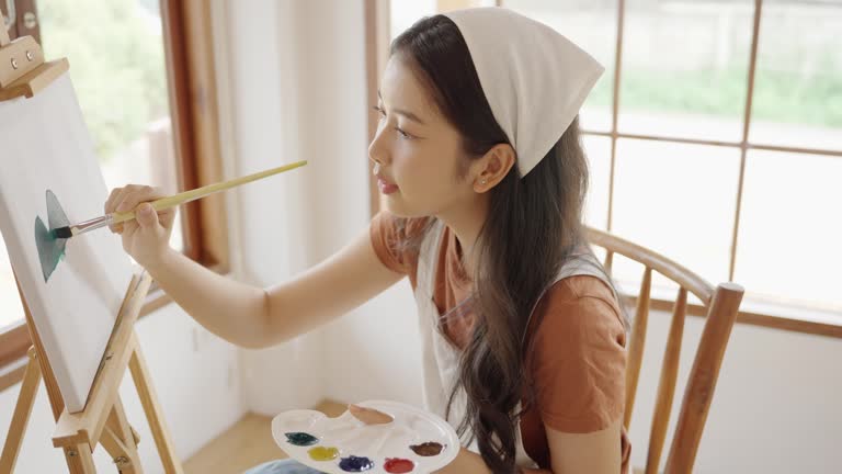 Asian young talented woman artist coloring on painting board in house. Attractive beautiful female draw art picture, creating artwork with watercolor paint and brush enjoy creativity activity at home