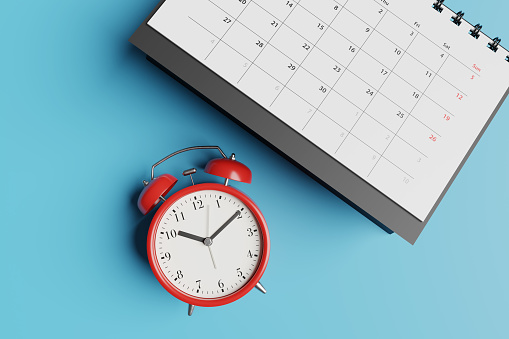 Black desk calendar and red alarm clock on blue background. Illustration of the concept of tight schedule, deadlines, due dates and workload