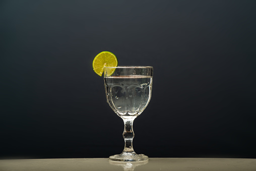 a glass cup with clear water and a lemon on the rim.