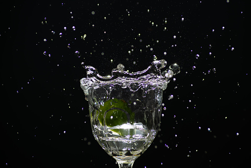 a slice of lemon falling into a glass cup with clear water causing splashes.