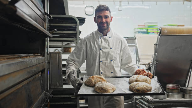 istock Baker cook tasty warm bread loaf at bakery. Smiling man portrait. Bake fresh bun 2148382025