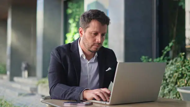 Handsome 30s top manager work laptop. Entrepreneur type computer macbook. Business man look monitor. Young male businessman. Urban city background. 40s employee create start up. Ceo office boss job.