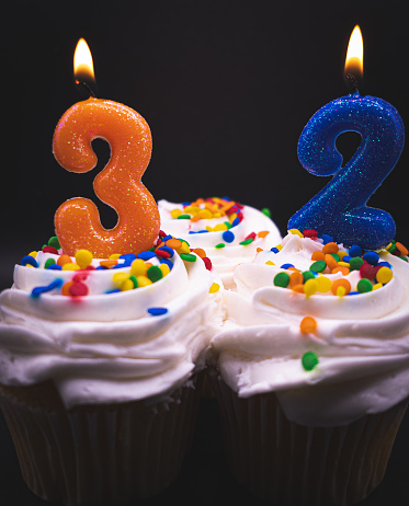 Age 32 candles on vanilla funfetti cupcakes on a black background