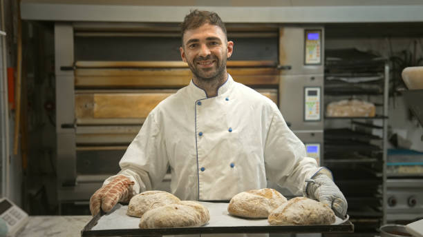 istock Baker man hold tray with fresh baked bread loafs at bakery. Smiling guy portrait 2148382768