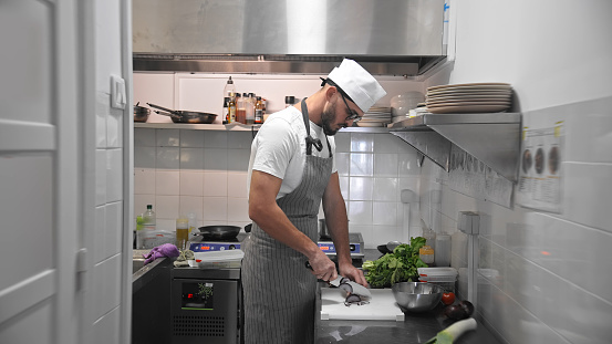 Male head chef prepare tasty fresh dish. Man cook meal restaurant kitchen. Young adult person work at cafe cuisine wear white hat. Guy make diet lunch food. Culinary worker job. Cookery staff uniform.