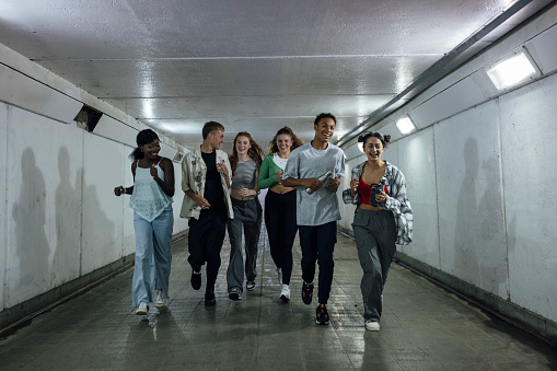 A wide angle front view of a group of young teenage friends who are walking through an underpass together as they head down to Newcastle upon Tyne Quayside. They are smiling and chatting and checking their mobile phones as they walk through the tunnel.
