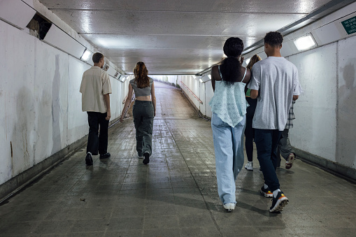 A wide angle rear view of a group of young teenage friends who are walking through an underpass together as they head down to Newcastle upon Tyne Quayside. They are smiling and chatting and checking their mobile phones as they walk through the tunnel.