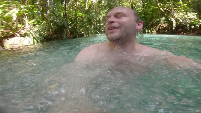 Man submerged underwater, surrounded by bubbles, then surfacing In The Kali Biru (Blue River) Within Tropical Forest in Raja Ampat, West Papua, Indonesia.