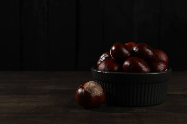 Brown chestnut fruits in a black bowl on a dark background