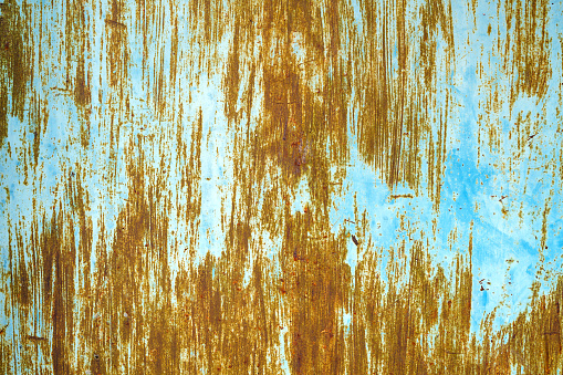 On a rusty metal-plated flat steel surface, there are areas where blue paint has peeled off.