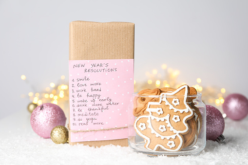 Cookies in jar and paper with list on box on light background