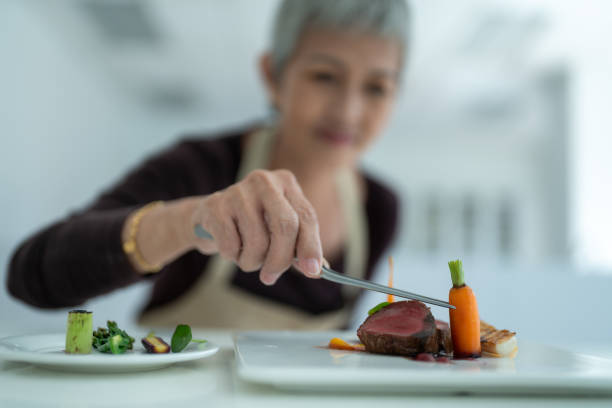 Senior adult female student trying to do plate decoration. Learning from professional culinary school.