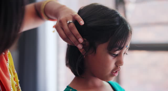 Indian mom brushing child hair in living room of family home with traditional outfit. Love, care and young mother with girl kid getting ready with hairstyle in culture clothes or fashion at house.
