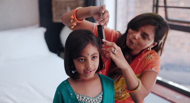 Indian mother brushing kid hair in living room of family home with traditional outfit. Love, care and young mom with girl child getting ready with hairstyle in culture clothes or fashion at house.