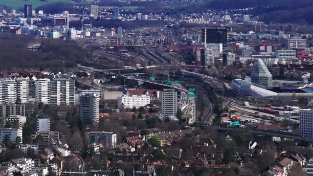 Aerial footage of transport infrastructure in city. Busy highway and multitrack railway line leading around football stadium and residential urban borough. Basel, Switzerland