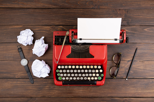 Writer or journalist workplace - vintage red typewriter, glasess and notepad on the wooden desk, top view