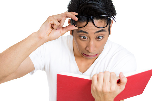 portrait of young man, with wide opened eyes staring at a book page, shocked, surprised by the twists and turn of story, isolated on white background.