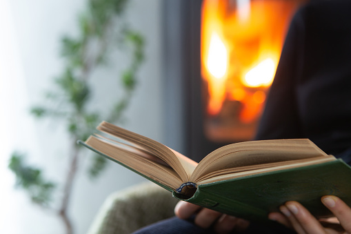 Female reading a book by the fireplace. Cozy winter lifestyle