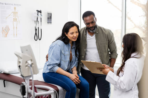 Unrecognizable female doctor talks with the couple in her office The unrecognizable female doctor shows the couple the medical test results that they obtained recently from her other provider. human fertility stock pictures, royalty-free photos & images